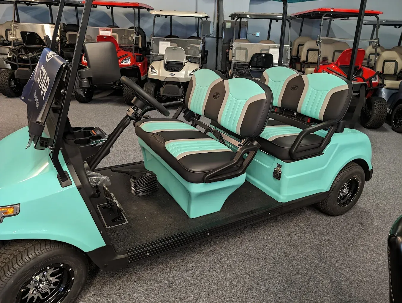 Turquoise golf cart with black seats parked among other golf carts indoors