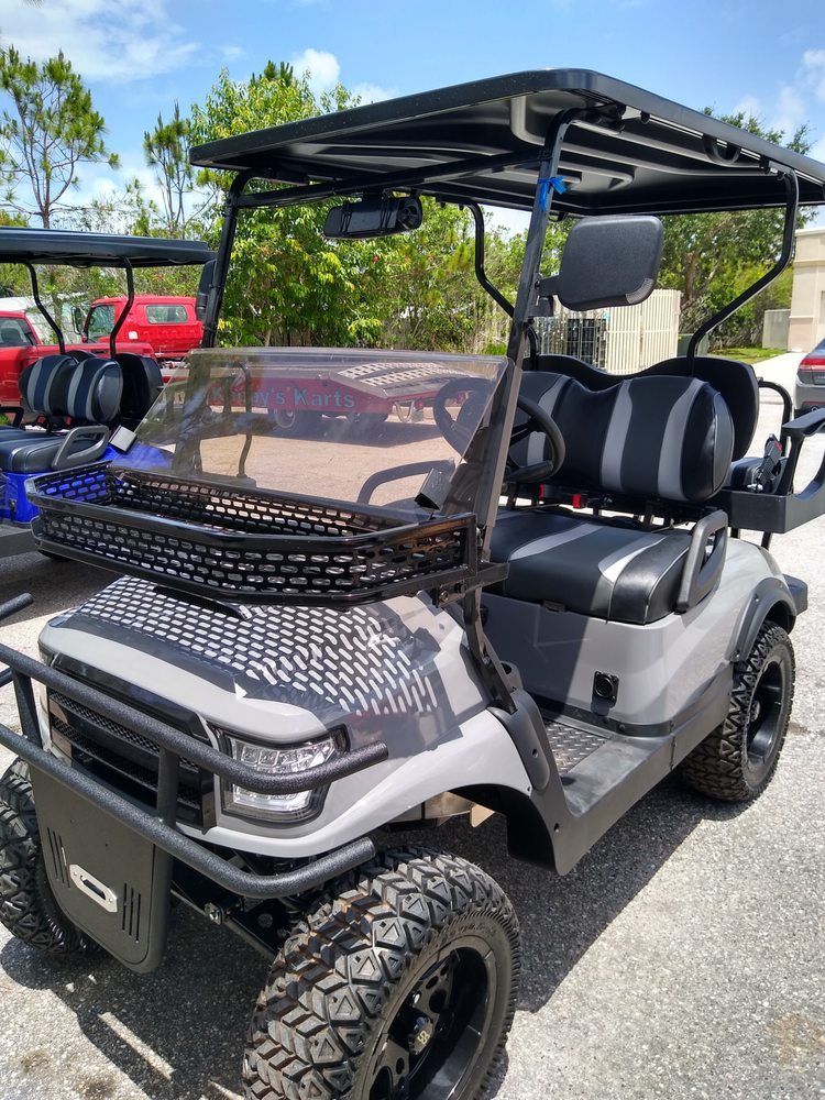 Gray golf cart with a black roof and mesh windshield parked outdoors in a lot