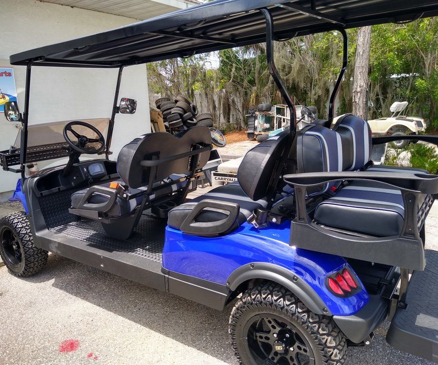 Blue and black golf cart parked outdoors under a black canopy, with empty seats and rear cargo area.