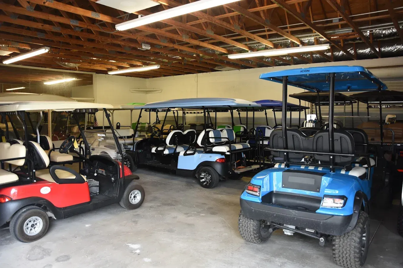 Several parked golf carts in a warehouse, including red, white, and blue carts with roofs.