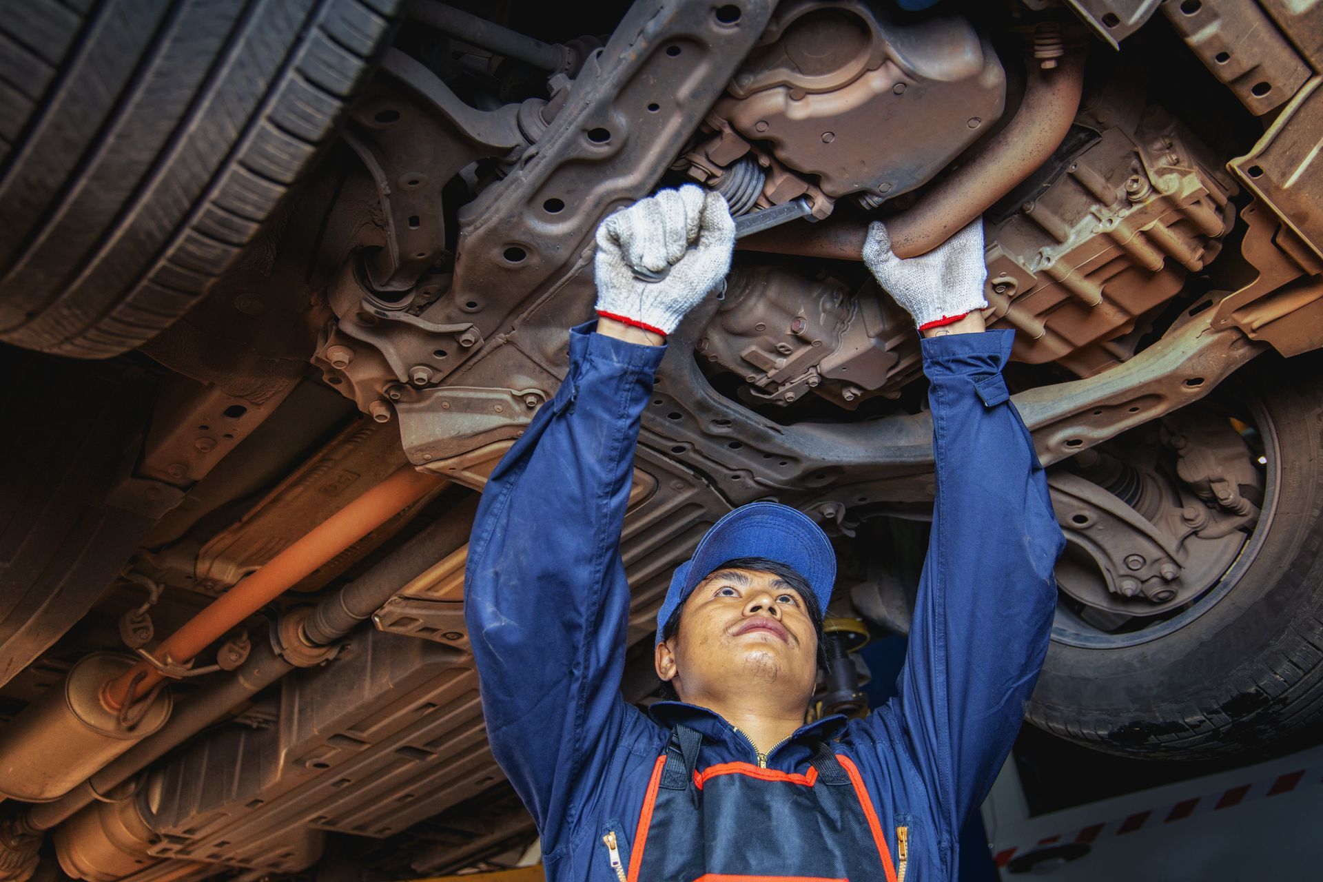 Auto mechanic inspecting car brake rotor under lifted vehicle in repair garage. Auto mechanic inspecting car brake rotor under lifted vehicle in repair garage.