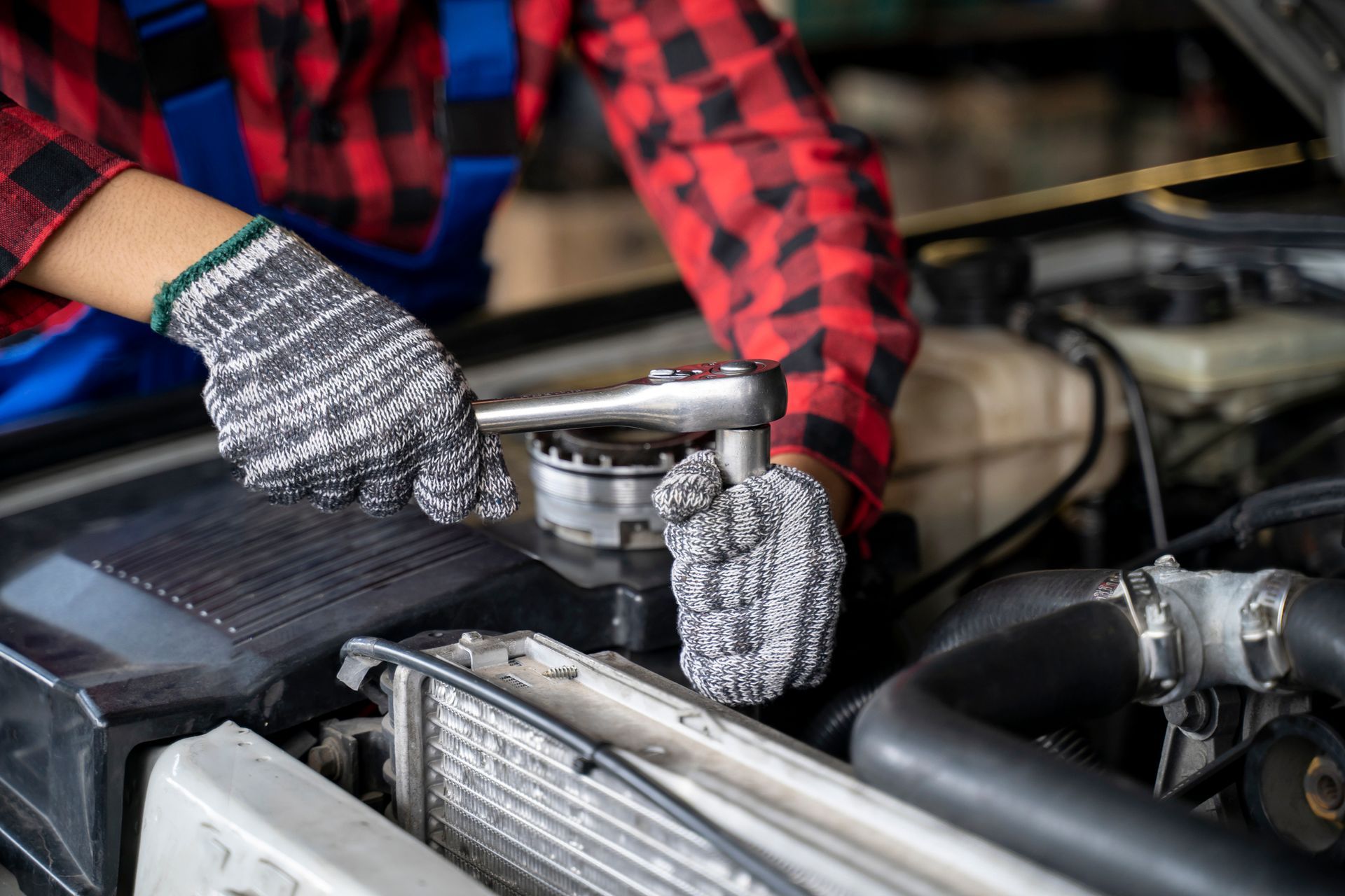 A mechanic wearing gloves repairing a car engine, focusing on transmission replacement service.