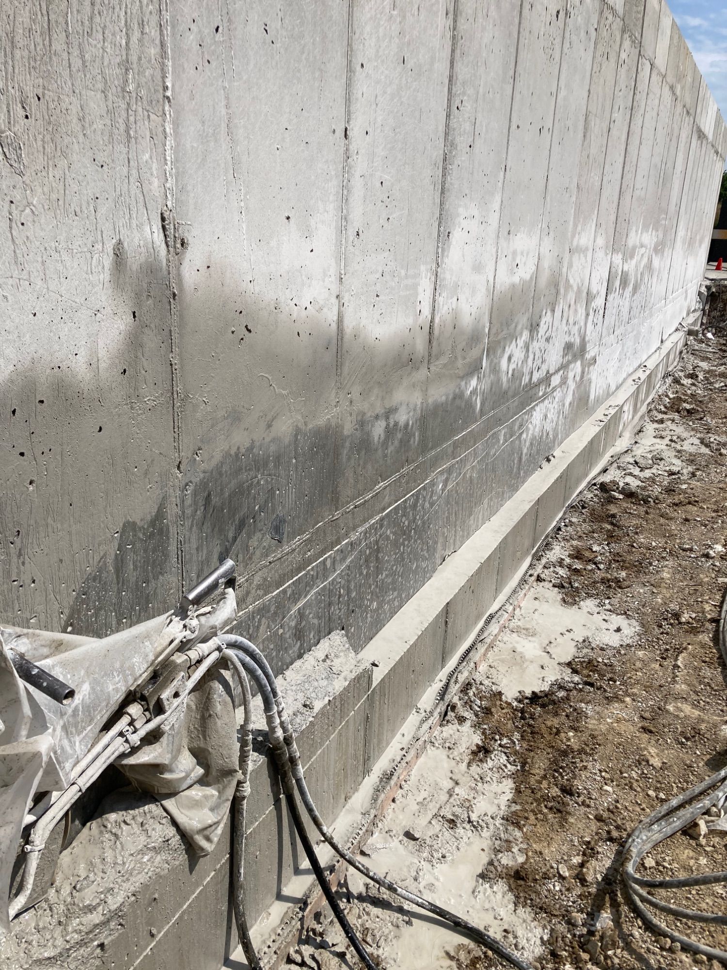 Concrete wall under construction; hoses, tools, and wet concrete visible.