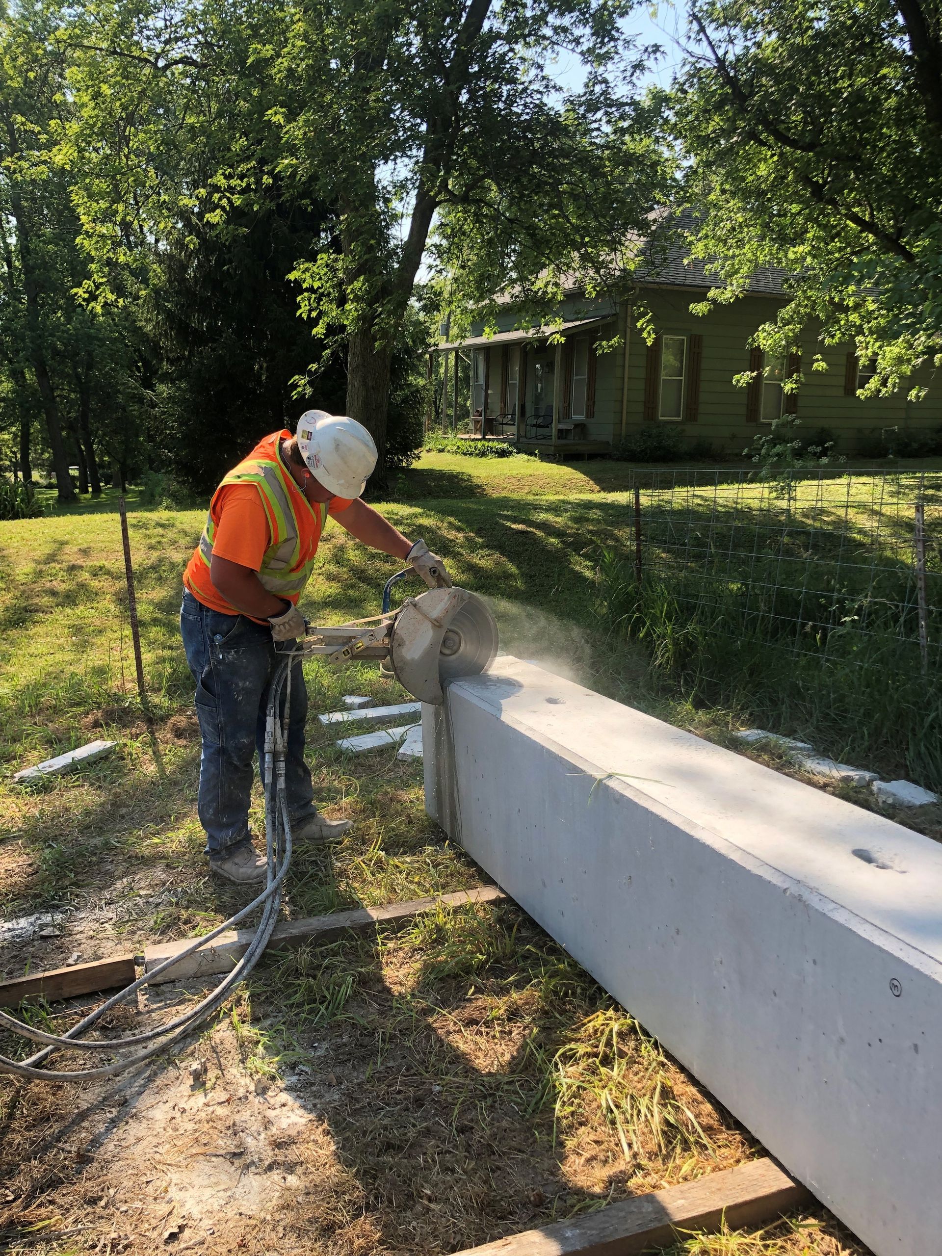 Construction worker in safety gear cutting concrete beam outdoors.