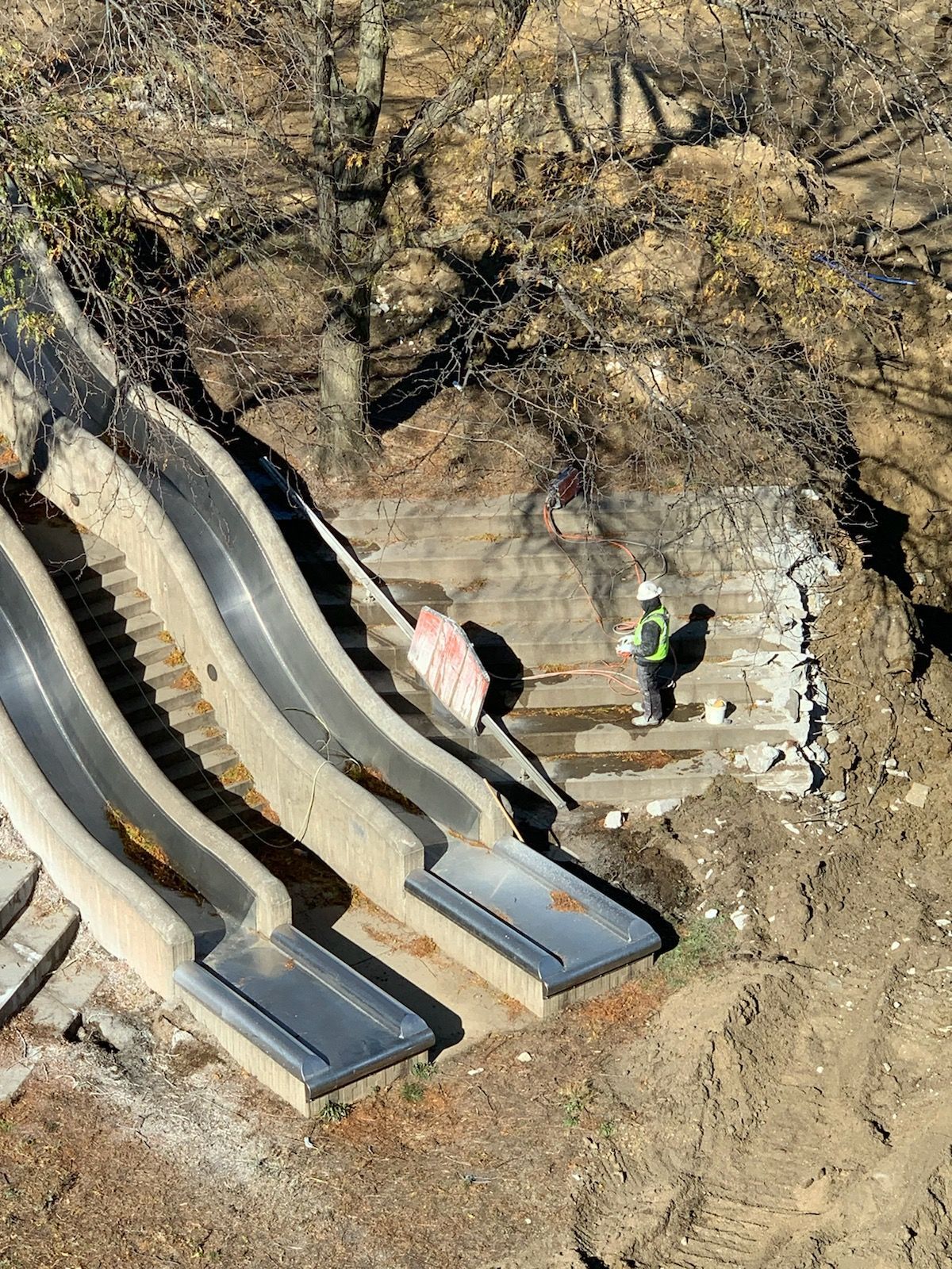 Two concrete slides with a worker in a hard hat; dirt surrounding the structure.