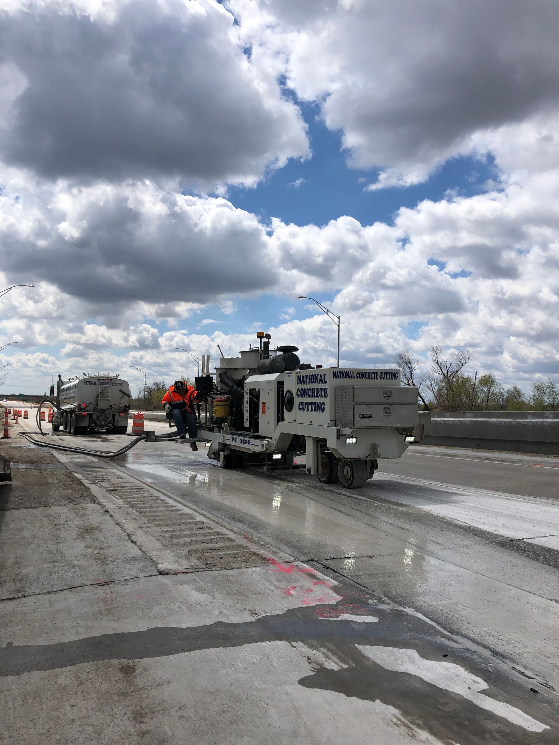 Construction crew using a machine to cut concrete on a bridge with cloudy sky.