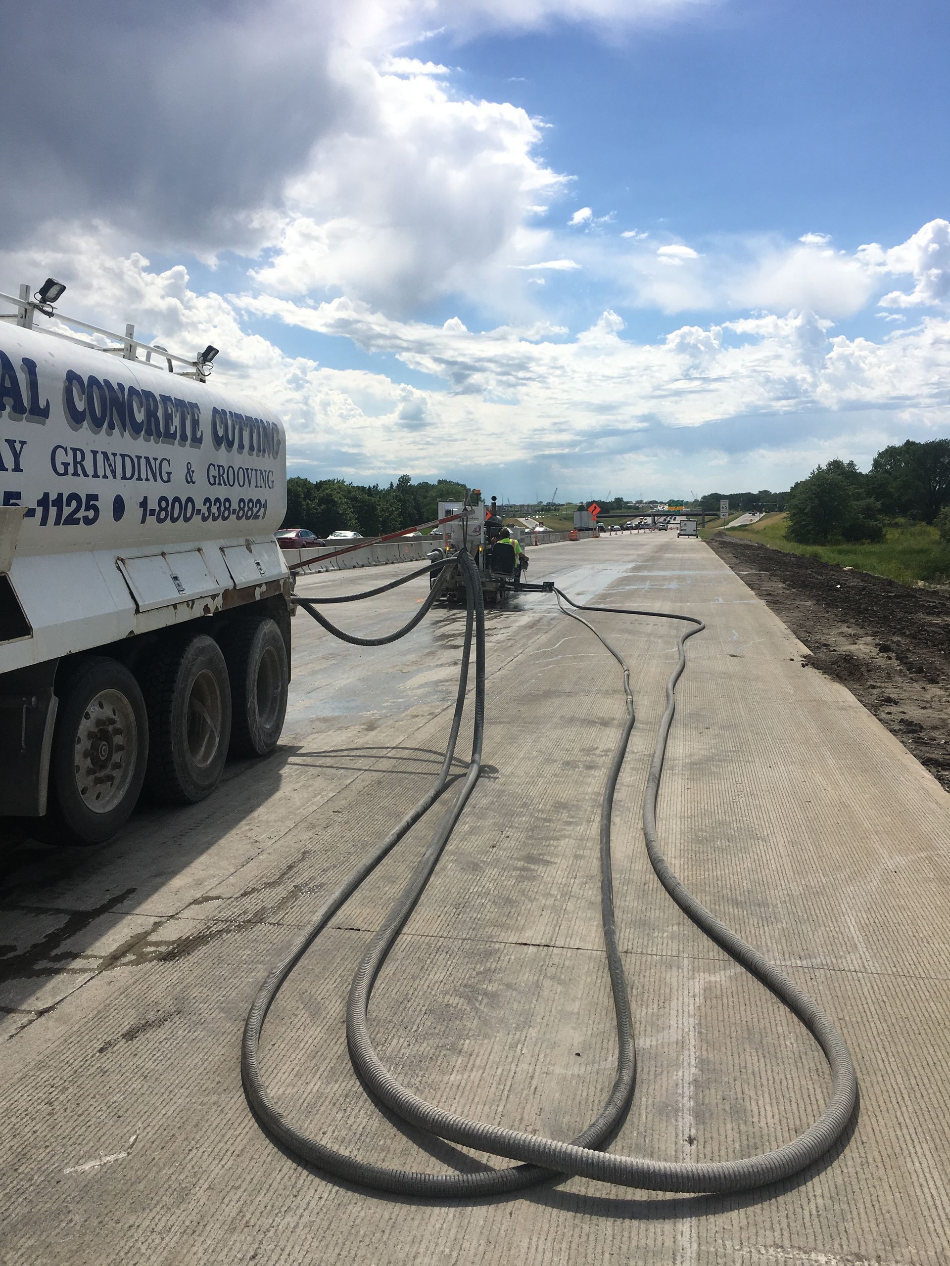 Concrete truck with hoses extending onto a new concrete road surface on a cloudy day.