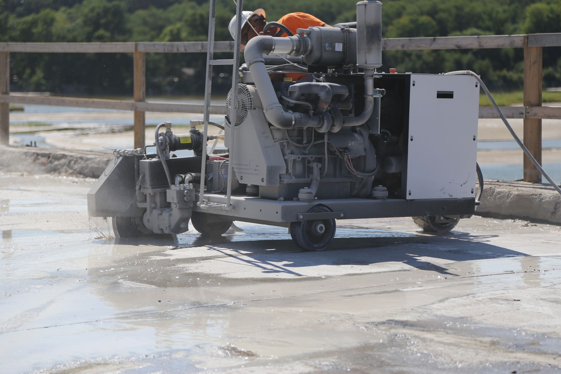 Construction worker operating a concrete saw on a bridge; generating water and dust.