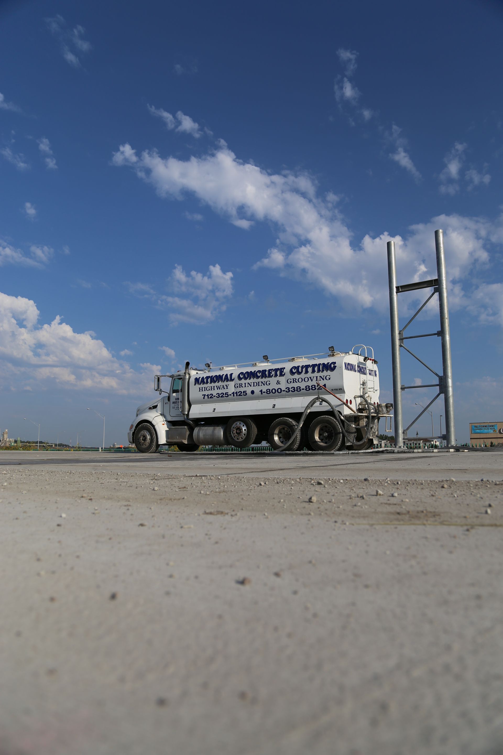 White sanitation truck on a concrete surface, blue sky with clouds in background.
