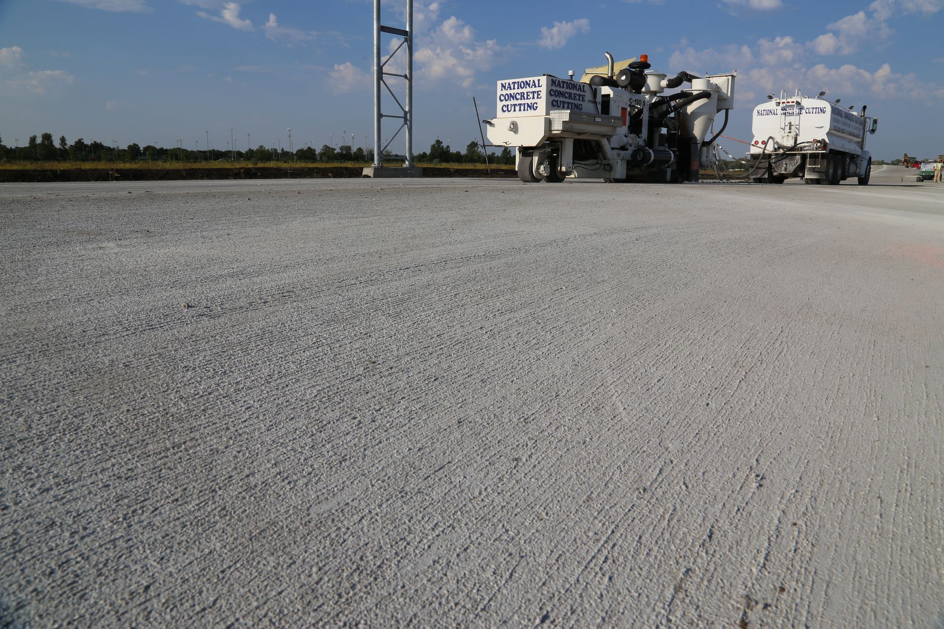 Concrete road surface with construction vehicles in the background on a sunny day.