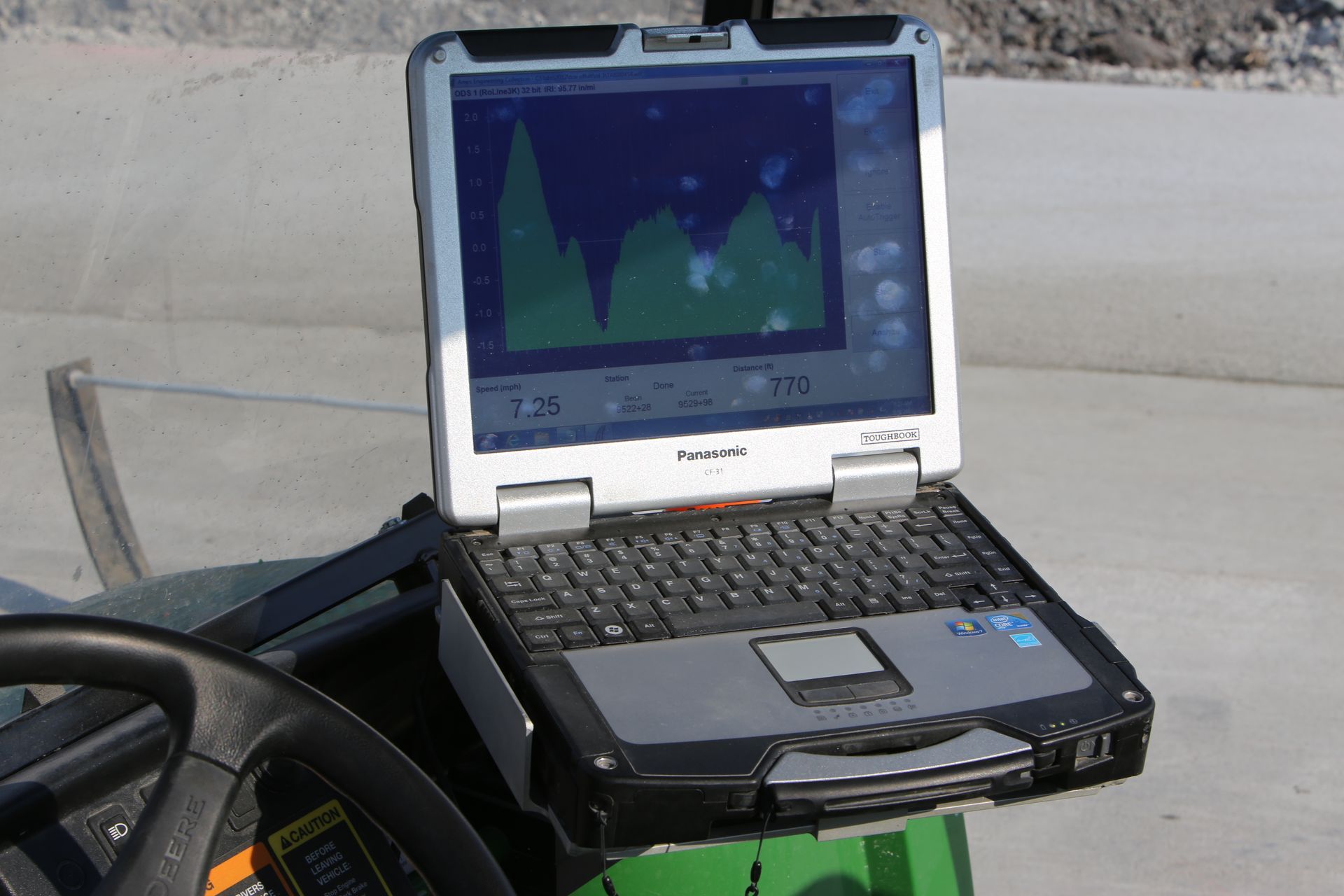 Laptop displaying a green graph is mounted on a golf cart-like vehicle, presumably for data collection outdoors.