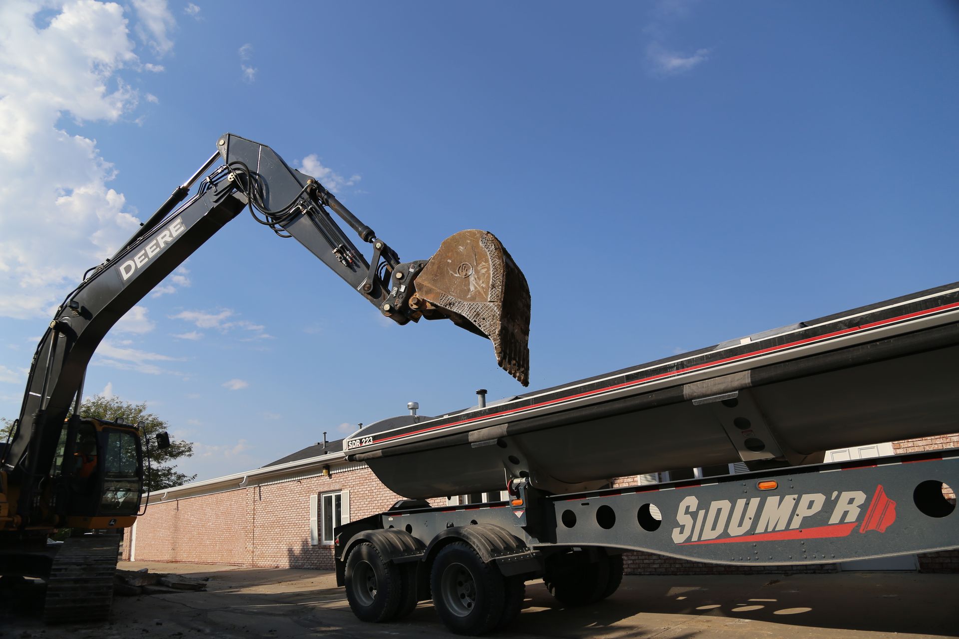 Excavator loading a dump trailer with a bucket. Sunny outdoor setting.