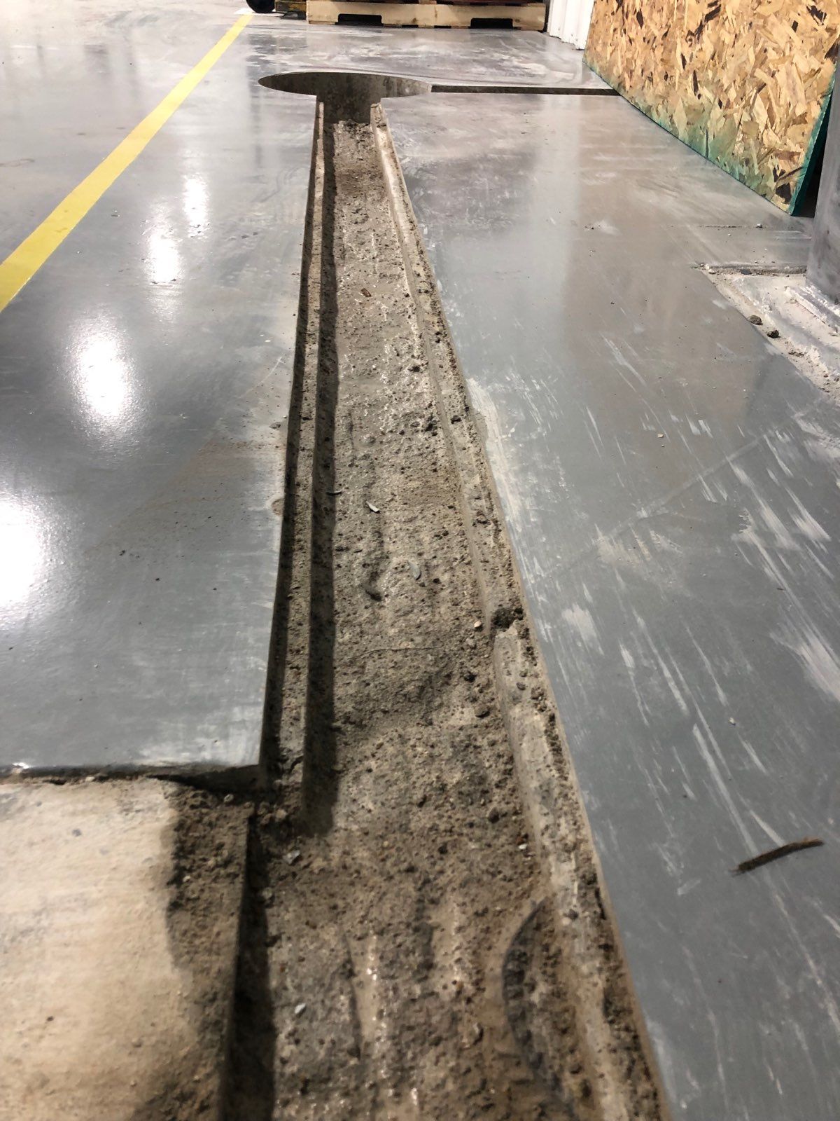 Open trench in a factory floor; gray metal flooring with a yellow line.