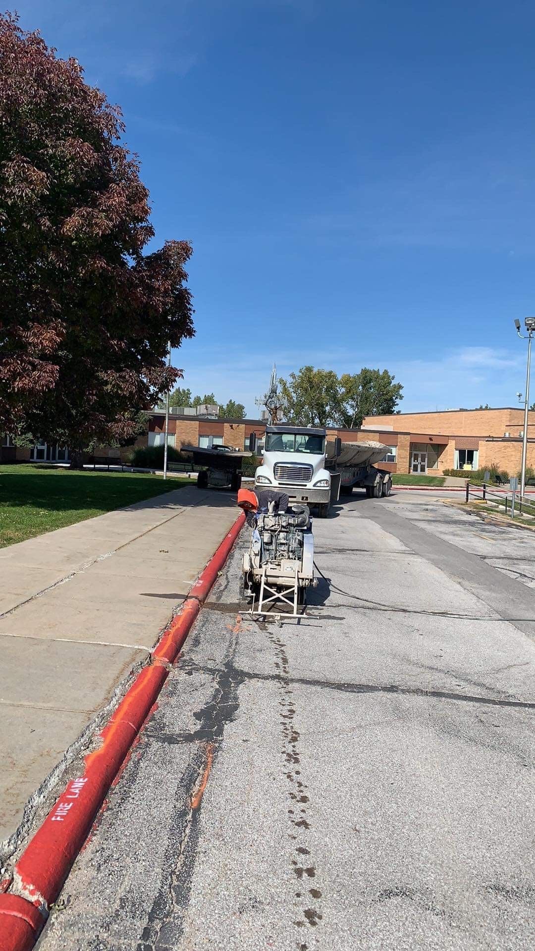 Roadwork on asphalt; red hose, saw, truck, and building. Sunny, blue sky.
