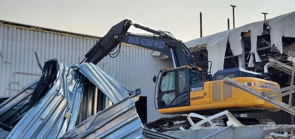 A yellow excavator demolishes a metal building.