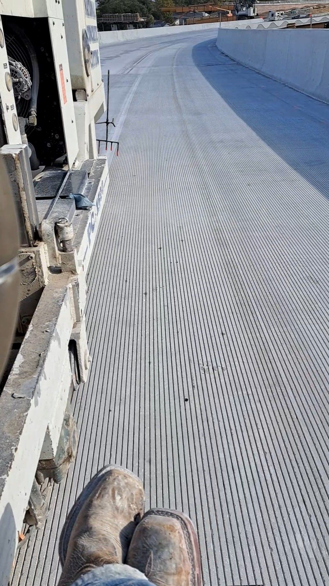 View from above of perforated metal surface, legs with work boots, and industrial equipment.