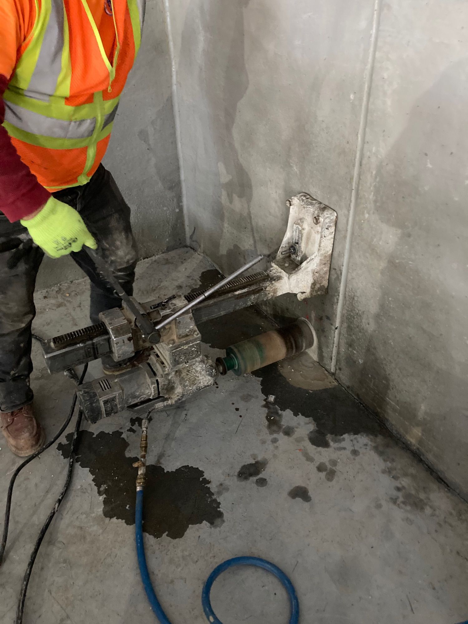 Worker using a core drilling machine on a concrete wall; construction site.