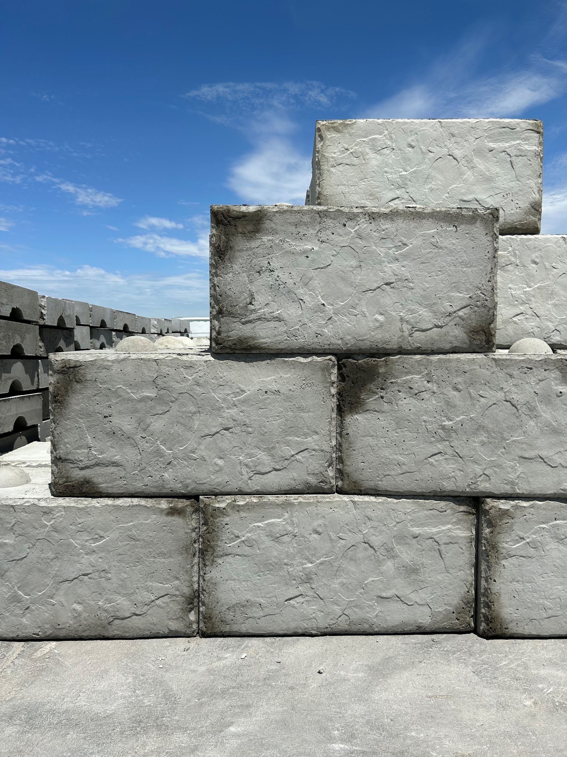 Stack of grey concrete bricks against a blue sky with some clouds.