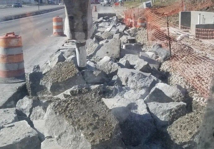 Breaker tool crushing concrete slabs at a roadside demolition site with orange safety fencing Breaker tool crushing concrete slabs at a roadside demolition site with orange safety fencing