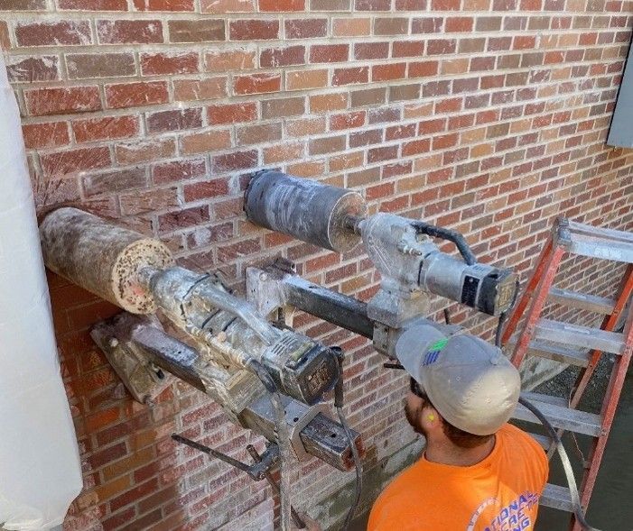 Worker operating two horizontal core drill rigs with diamond bits on a brick wall