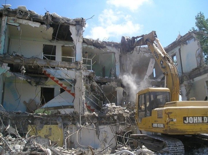 John Deere excavator demolishing a multi-story building with a hydraulic breaker John Deere excavator demolishing a multi-story building with a hydraulic breaker