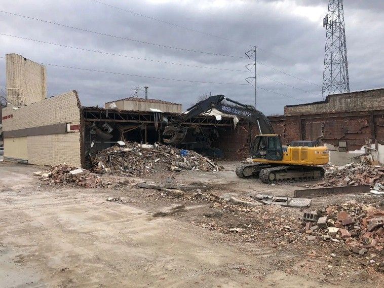 Yellow excavator demolishing a brick and tile building for National Concrete Cutting