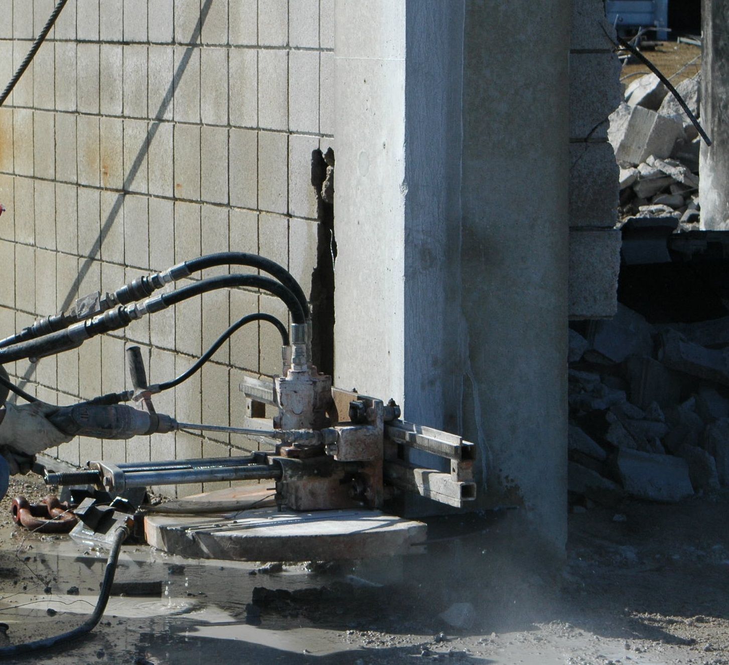 Concrete cutting saw in use, cutting through a concrete pillar at a construction site.