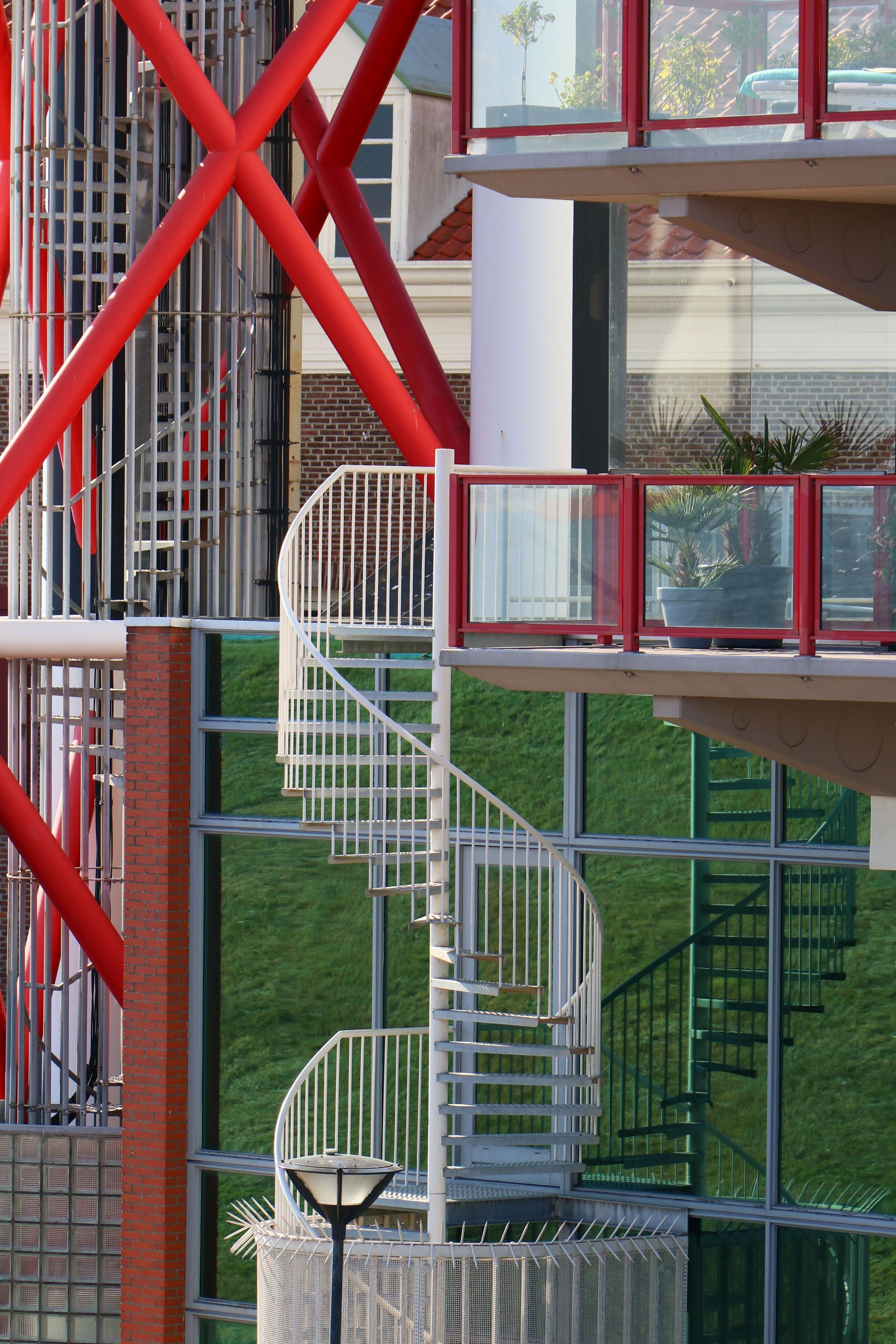 Outdoor white spiral staircase beside a modern building with red railings and large glass windows