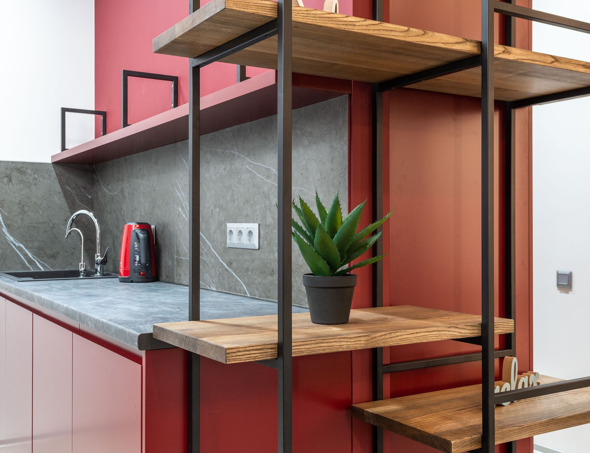 Modern kitchen with pink cabinetry, metal shelving, wooden shelves, and a potted plant on the counter.