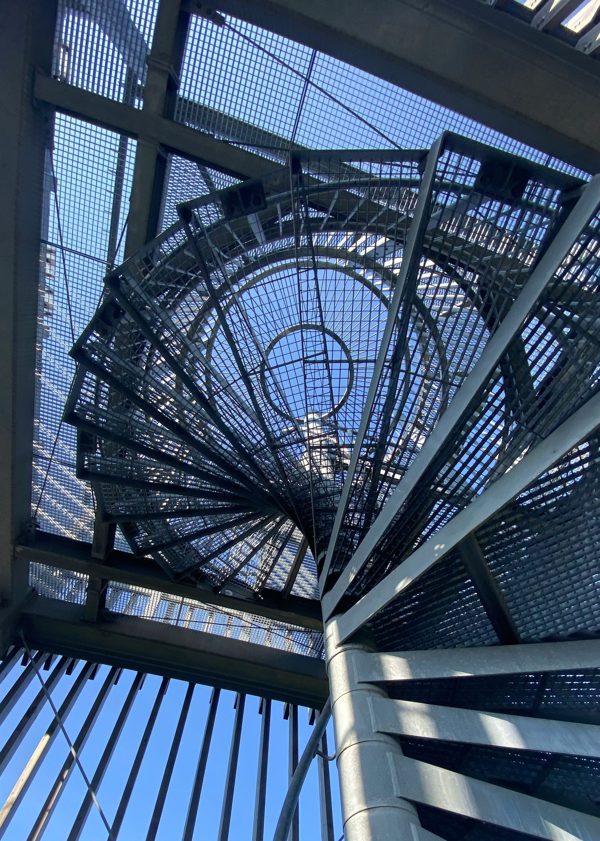 A low-angle view of a metallic spiral staircase with open-mesh steps