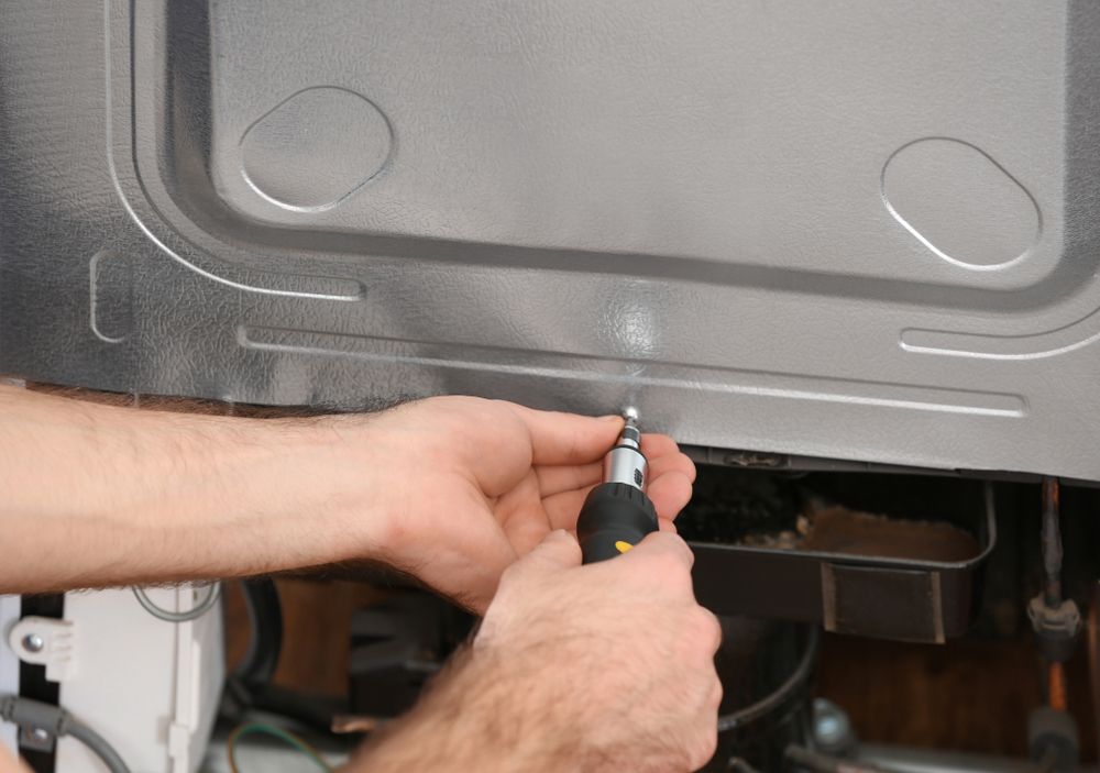 A Man is Fixing a Refrigerator With a Screwdriver — Davies Refrigeration & Air Conditioning in Warana, QLD