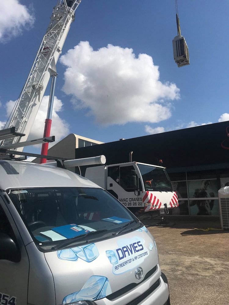 A Van With a Crane on Top of It is Parked in Front of a Building — Davies Refrigeration & Air Conditioning in Warana, QLD