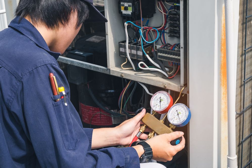 A Man in a Blue Shirt is Working on an Air Conditioner — Davies Refrigeration & Air Conditioning in Cooroy, QLD
