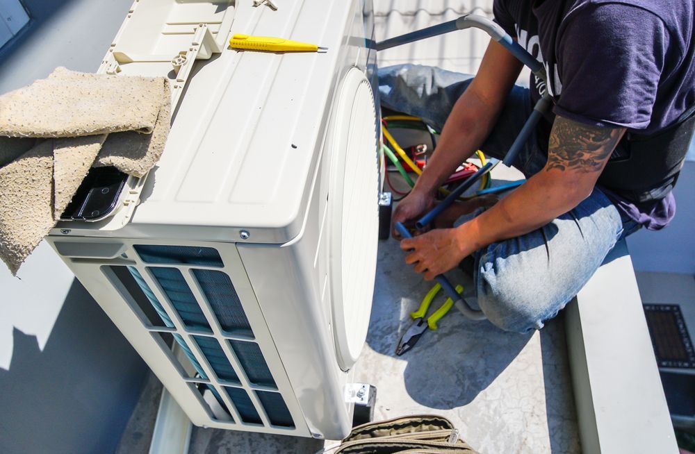 A Man is Fixing an Air Conditioner on the Roof of a Building — Davies Refrigeration & Air Conditioning in Warana, QLD