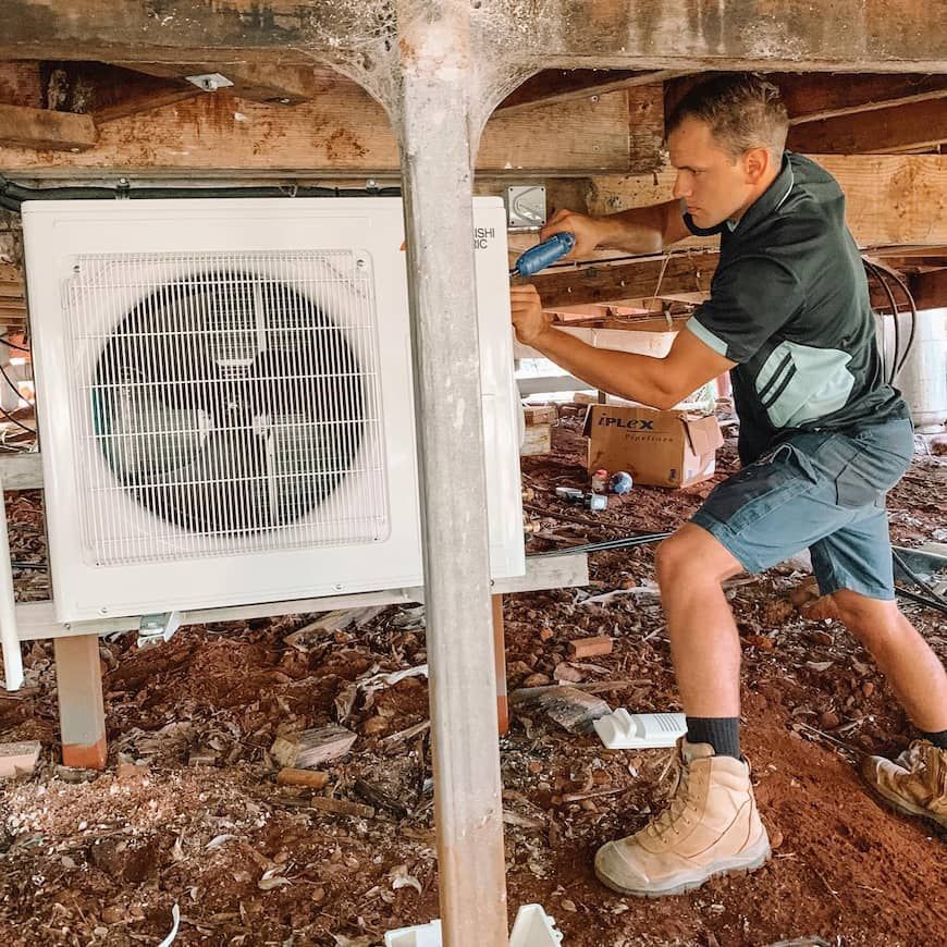 A Man installing an Air Conditioner Under a House  in Sunshine Coast — Davies Refrigeration & Air Conditioning in Warana, QLD