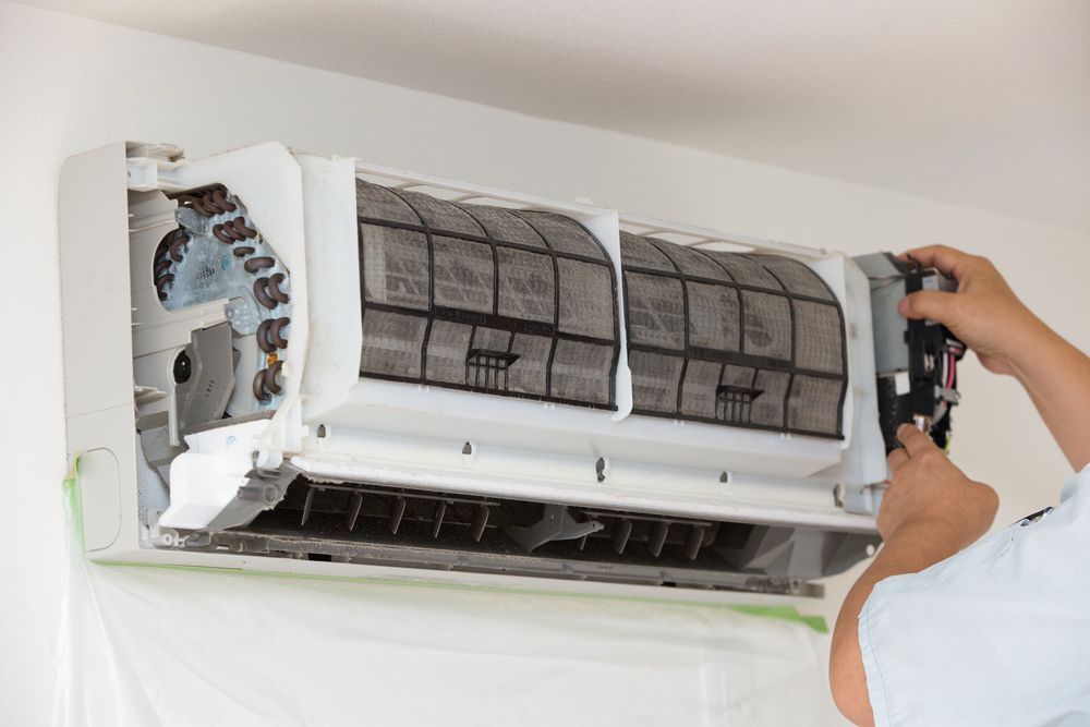 A Person is Cleaning an Air Conditioner With a Brush — Davies Refrigeration & Air Conditioning in Warana, QLD