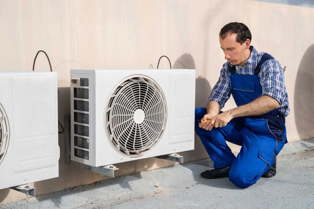 A Man is Kneeling Down Next to a Fan on the Side of a Building — Davies Refrigeration & Air Conditioning in Warana, QLD