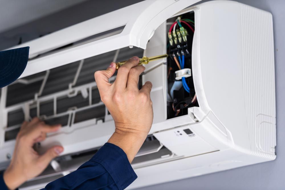 A Man is Fixing an Air Conditioner With a Screwdriver — Davies Refrigeration & Air Conditioning in Warana, QLD