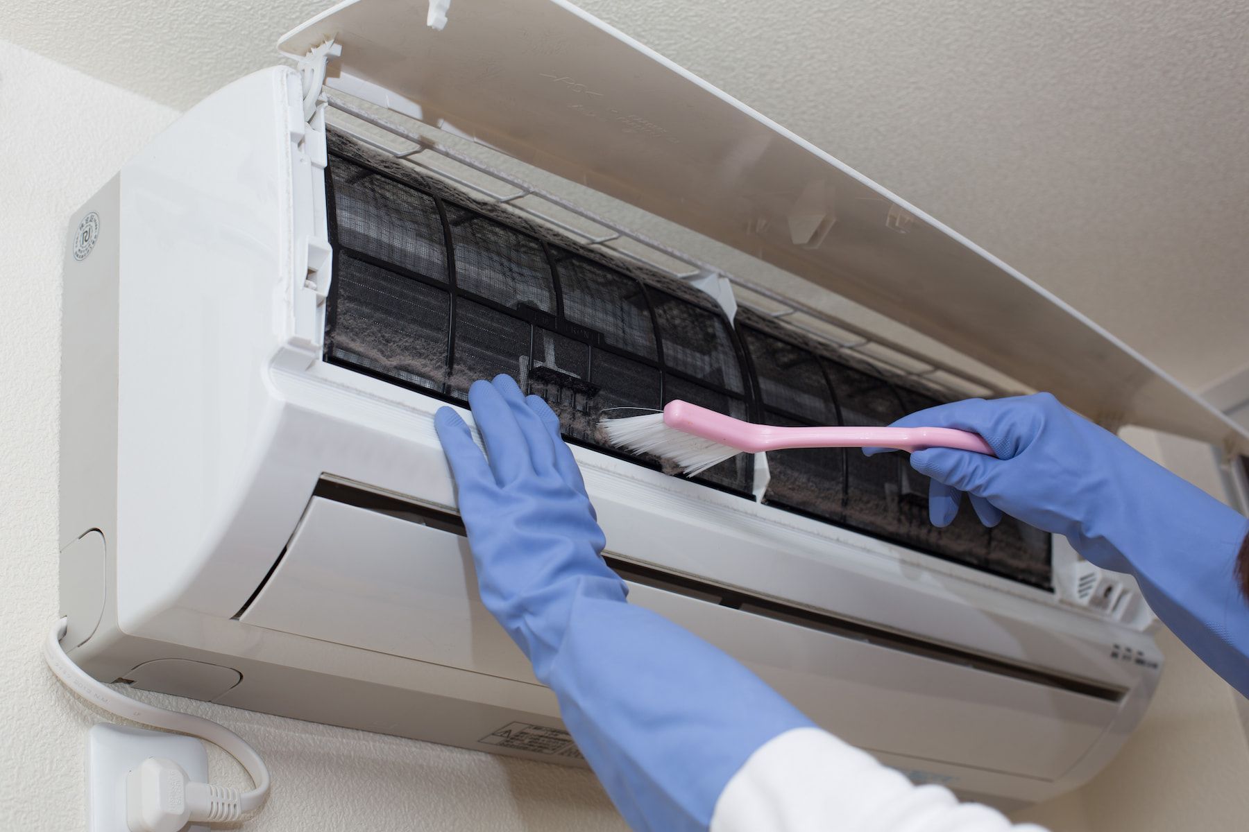 A Person is Cleaning an Air Conditioner With a Brush — Davies Refrigeration & Air Conditioning in Warana, QLD