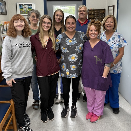 Group of seven smiling people posing indoors in a room with framed wall art.
