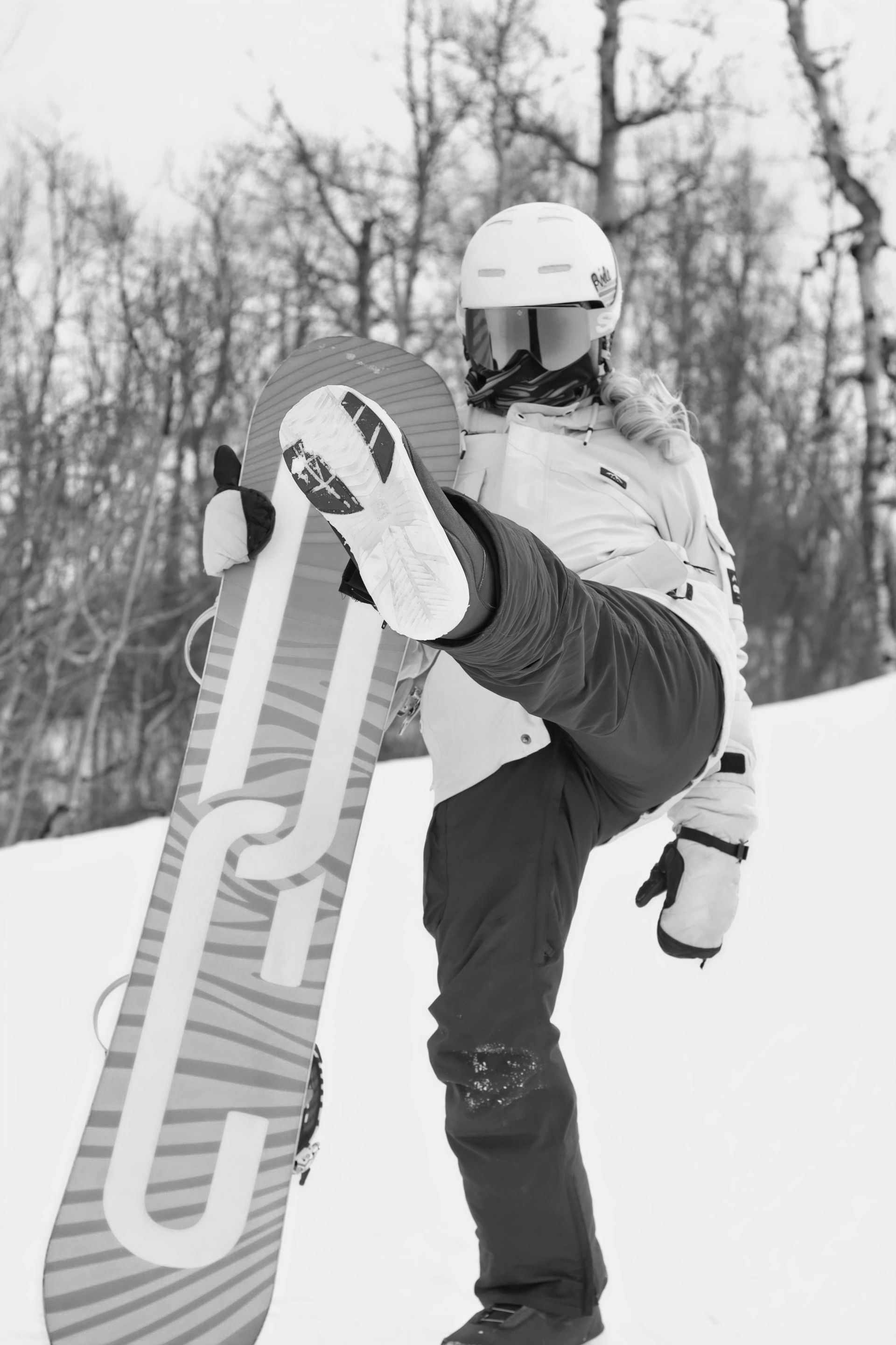 Snowboarder holding a board upright on a snowy slope, wearing a helmet and goggles.