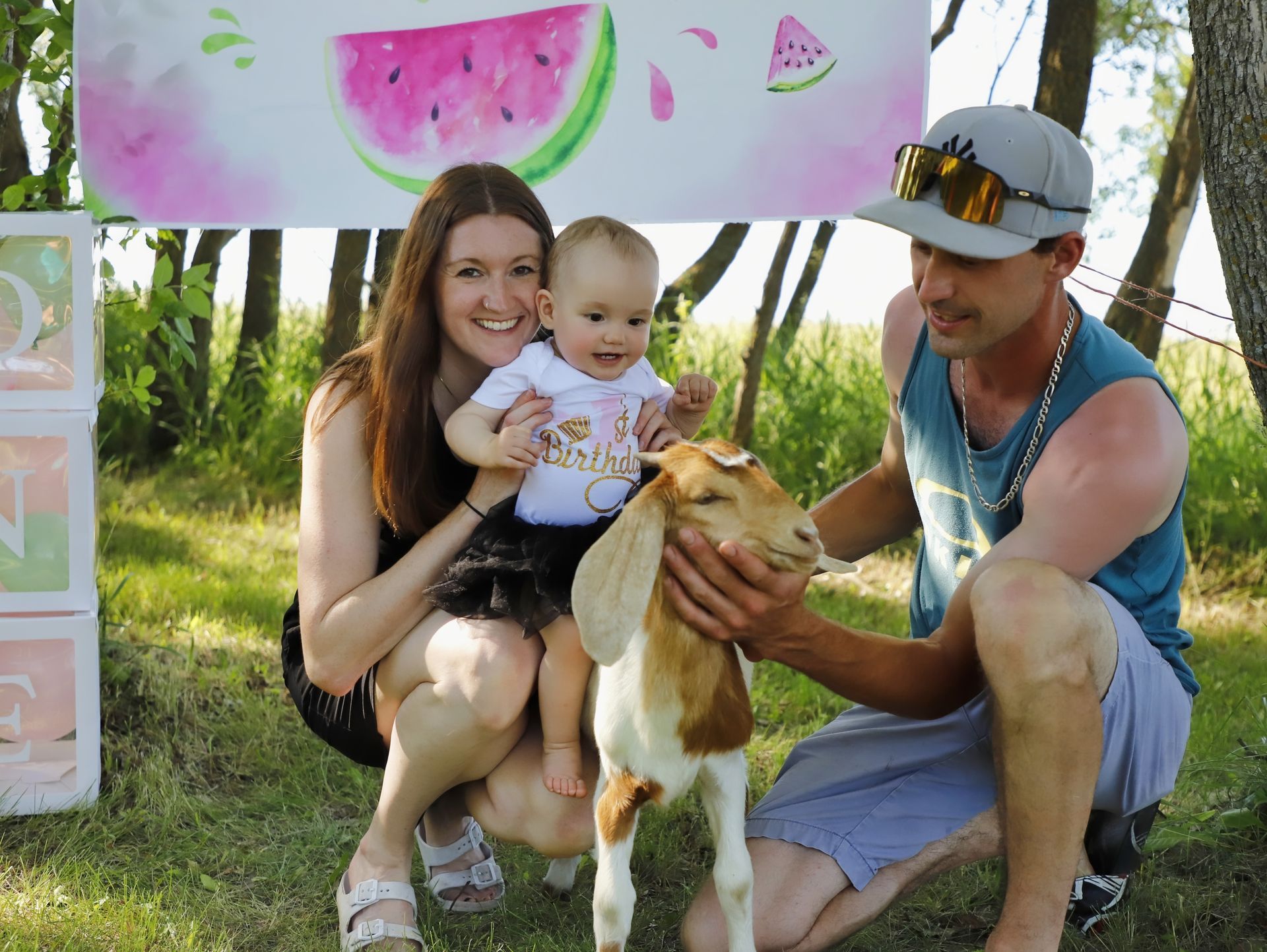 Family posing with a baby and a dog outdoors under a watermelon banner