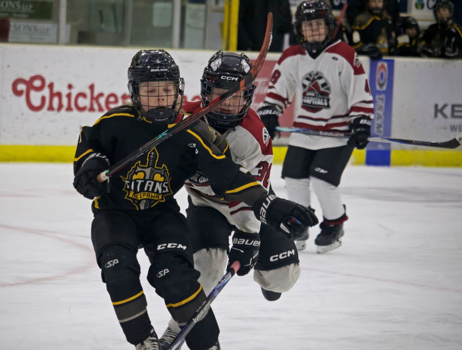 Black-and-gold hockey player skates toward camera in front of white-and-red opponents on an ice rink