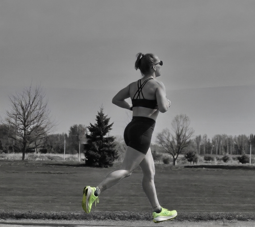 Runner in black sportswear jogging on a path with neon yellow shoes in a grayscale landscape.