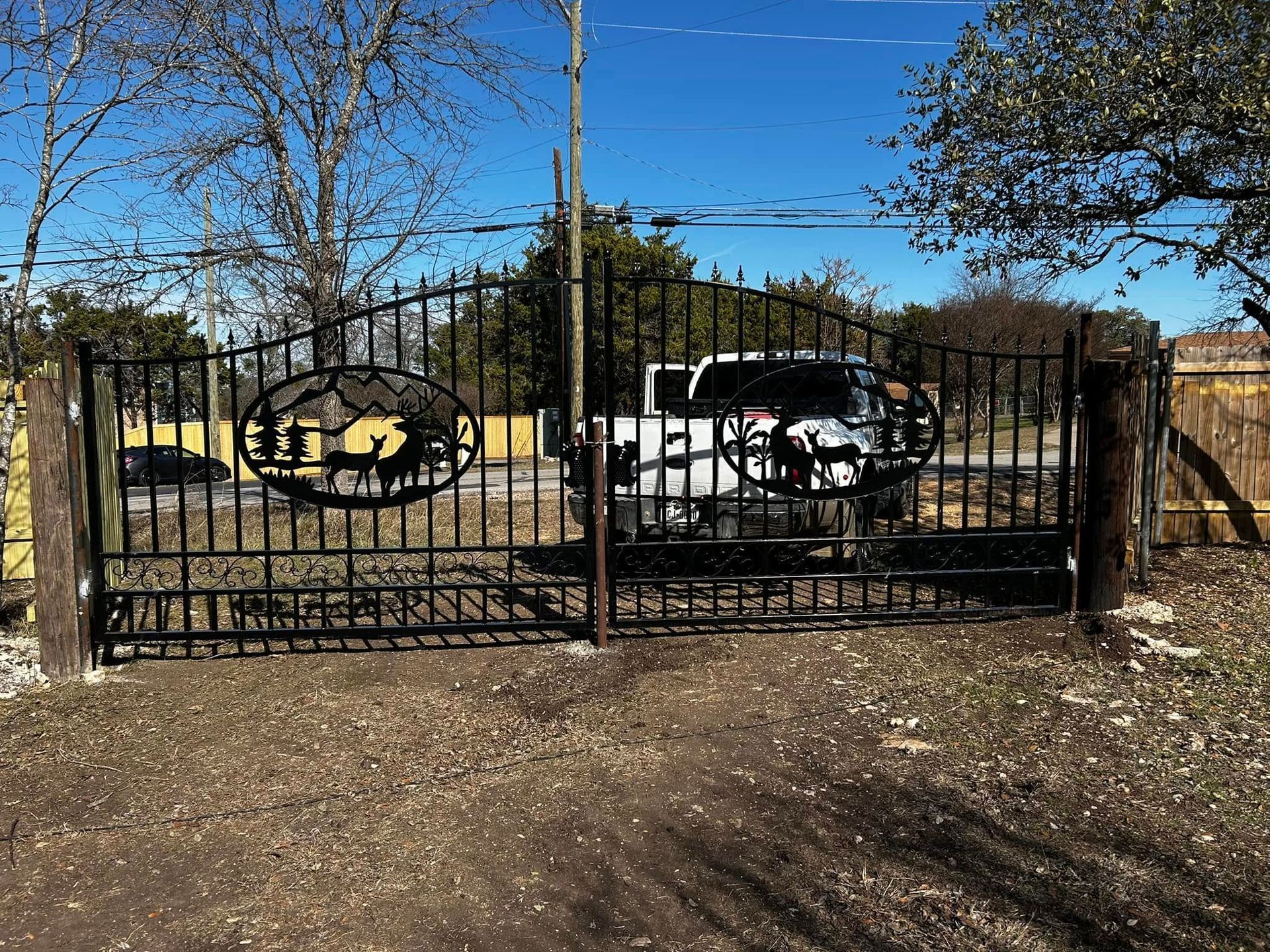 Black wrought-iron gate with decorative cutouts. A white pickup truck is behind the gate.