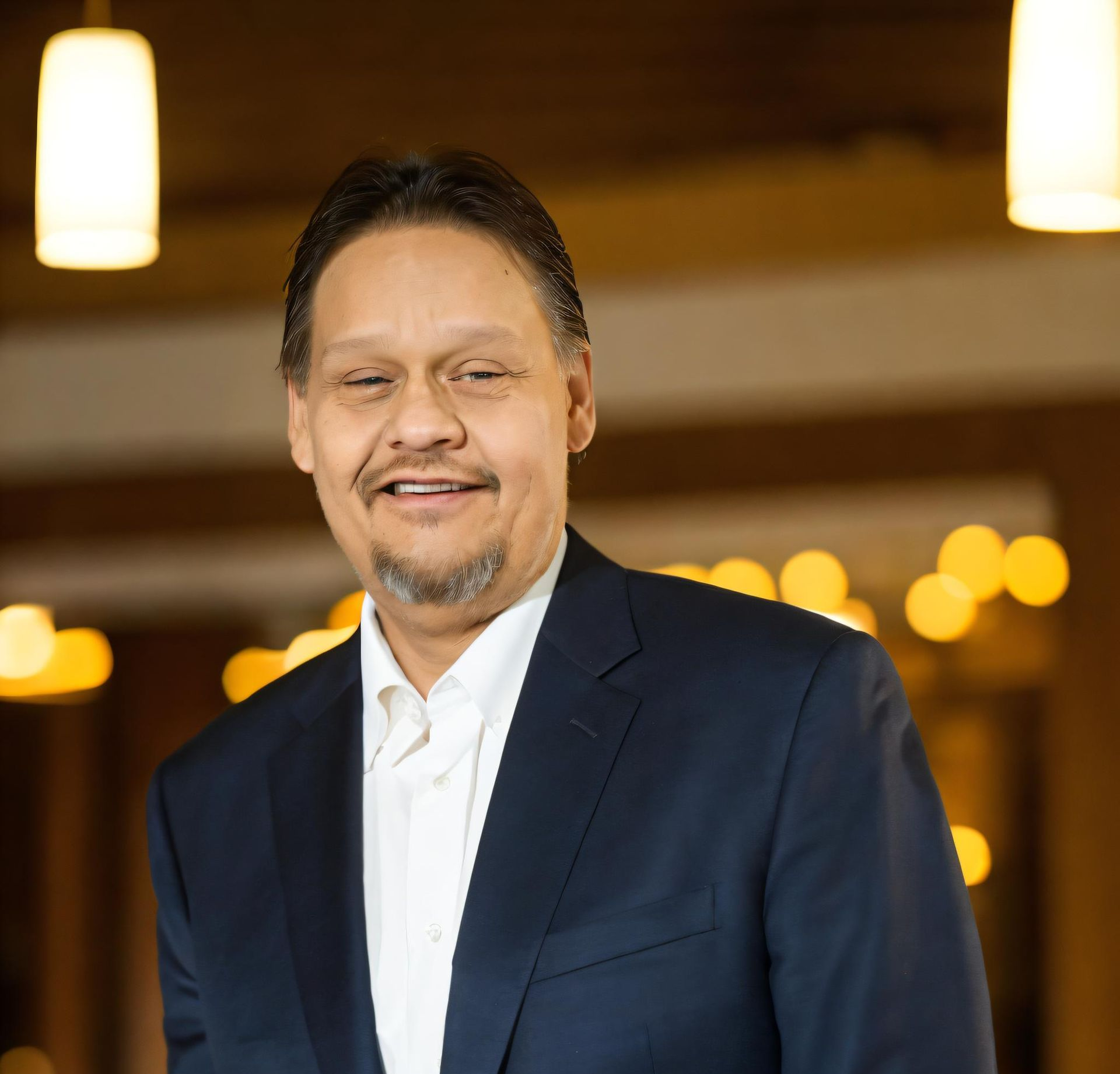 Tim Williams. Man in a navy blazer and white shirt, smiling, indoors with soft lighting.
