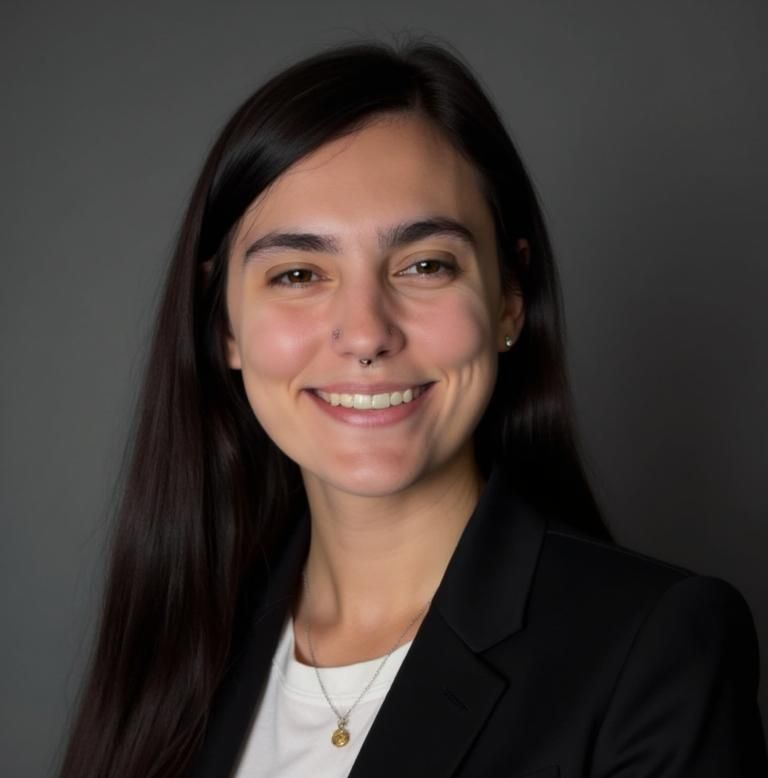 Woman with long dark hair, smiling, wearing a black blazer and white shirt. Gray background.