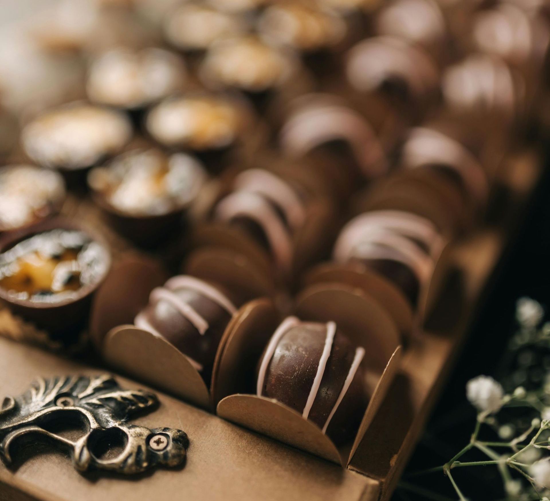 Rows of chocolate truffles, some drizzled with pink, on a wooden tray with decorative metal and flowers.