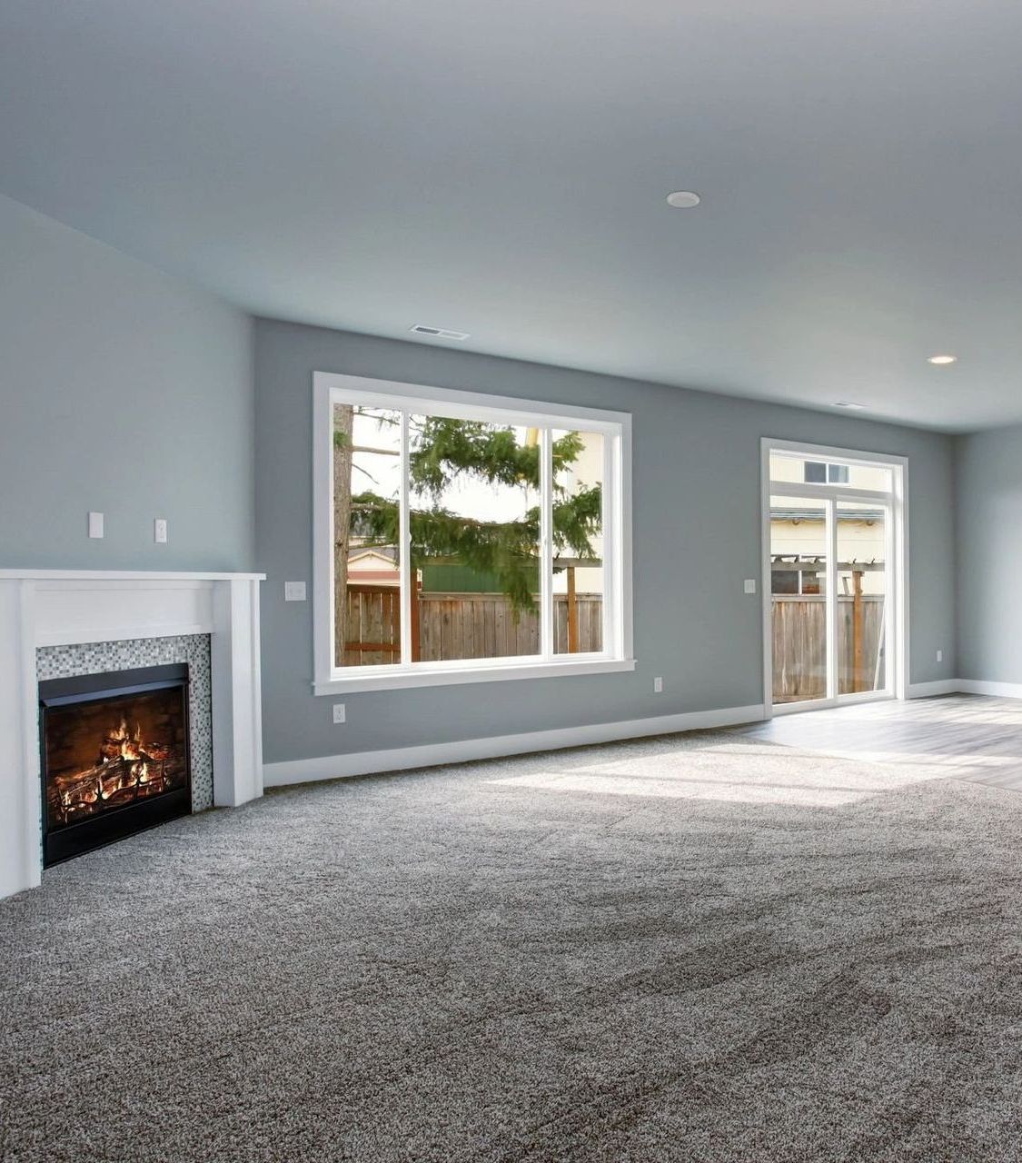 Empty living room with fireplace, window, and sliding glass door. Gray walls and carpet.