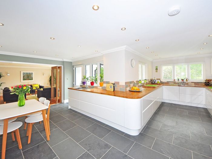 Spacious modern kitchen with white cabinetry, wooden countertops, gray tile floors, and a dining table.